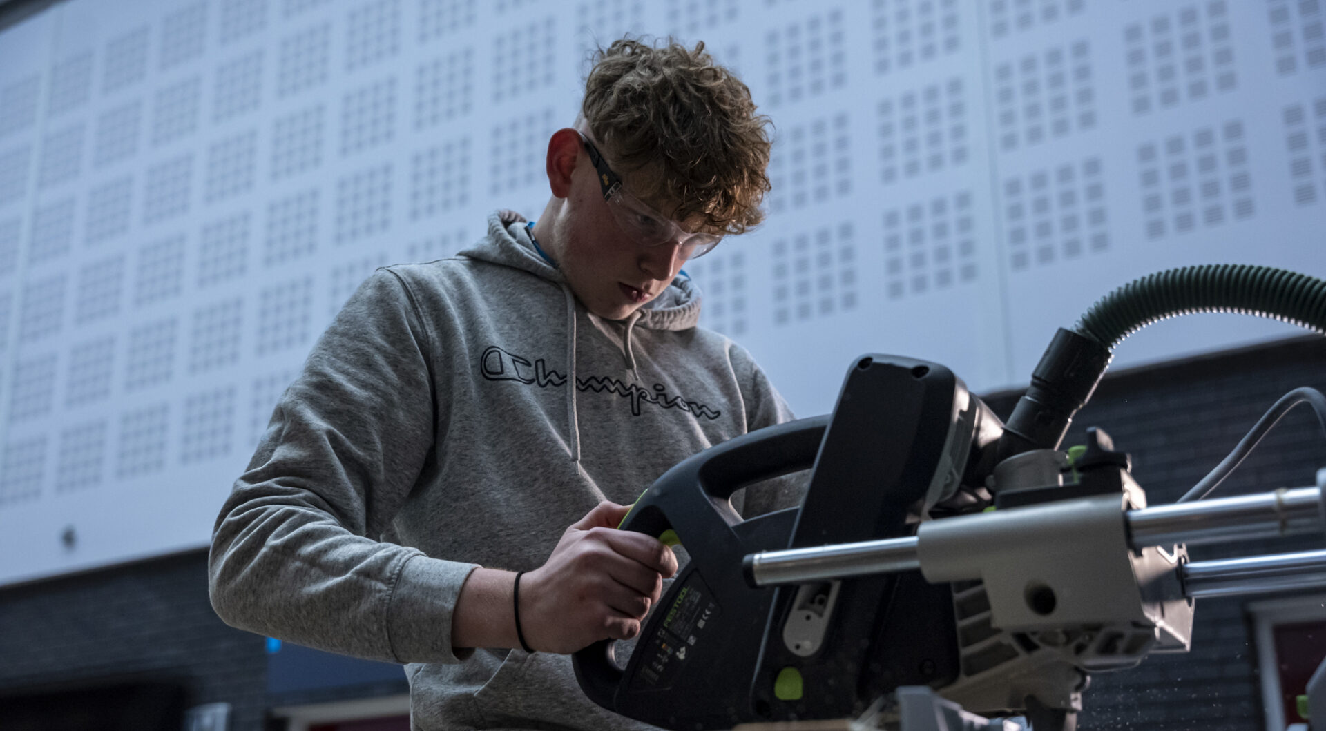 a construction student using equipment to cut some wooden materials to size