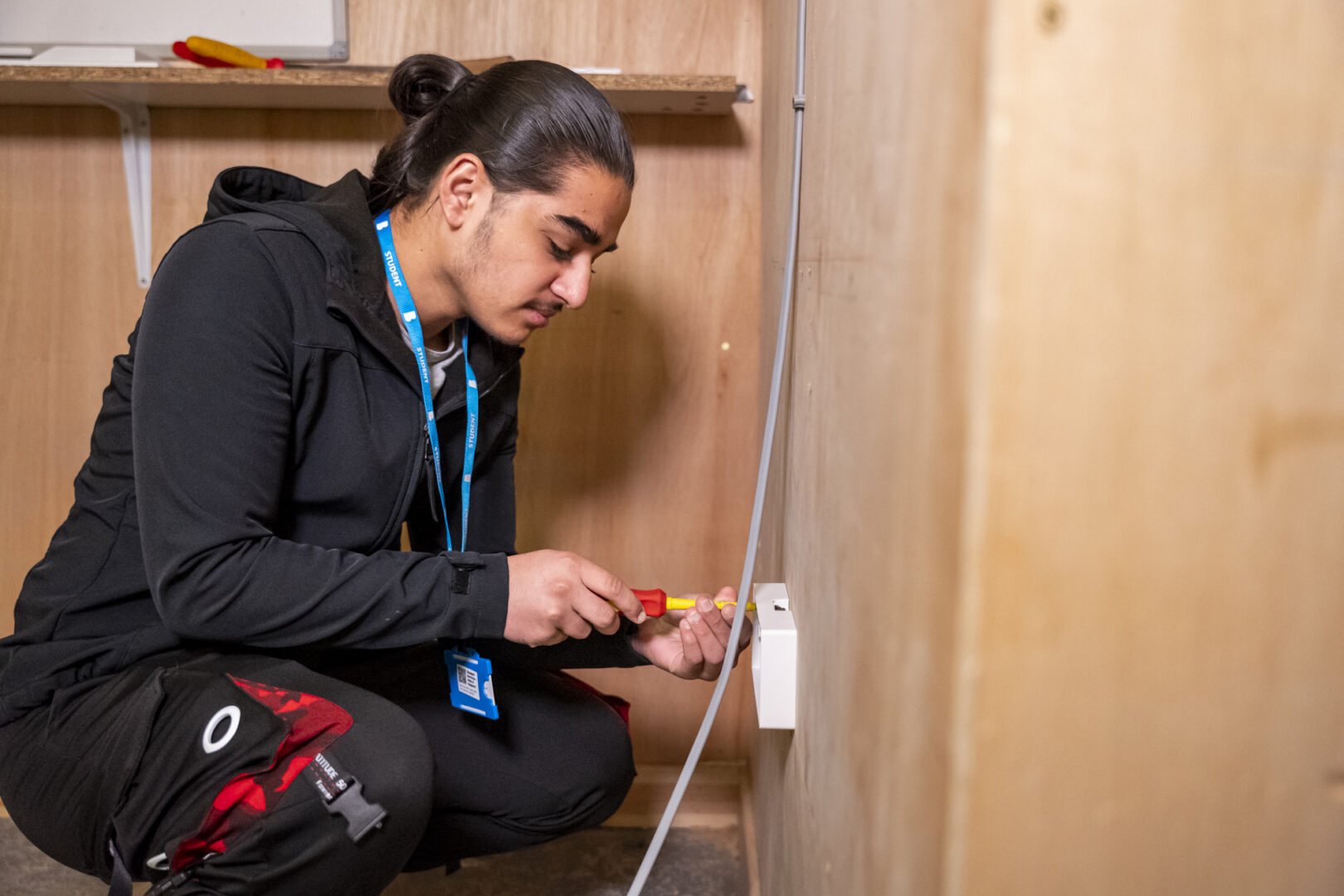 an electrical installation student knelt using equipment to check wiring