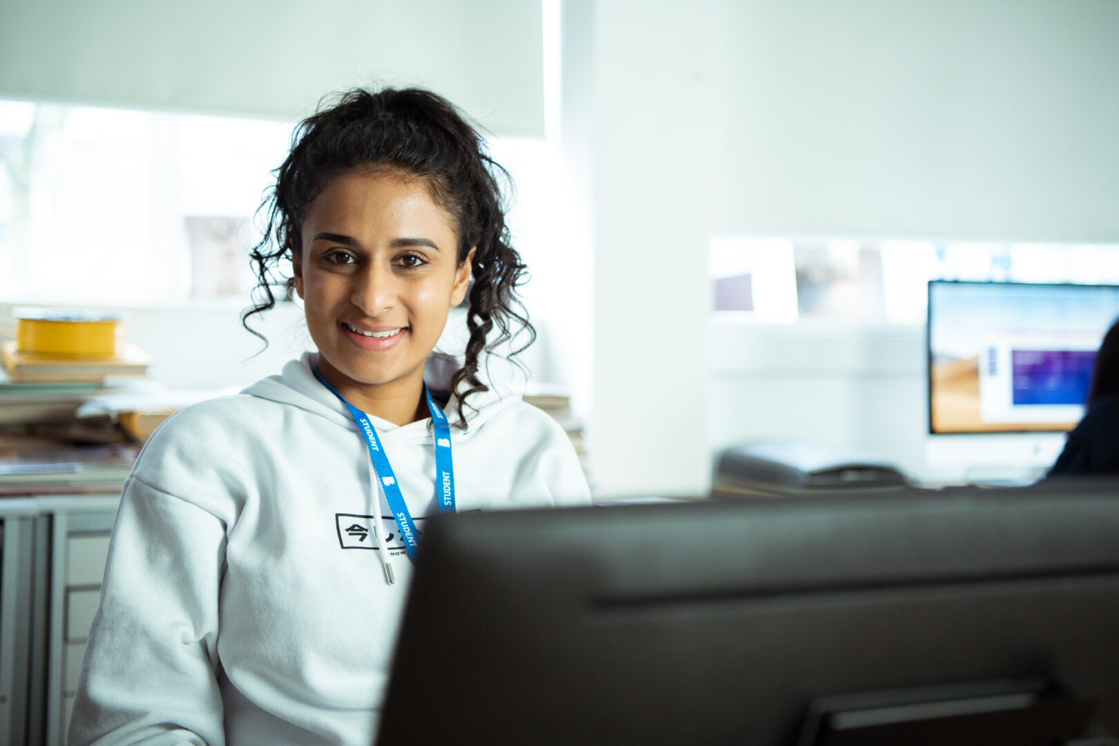 a smiling student sat at a desktop monitor