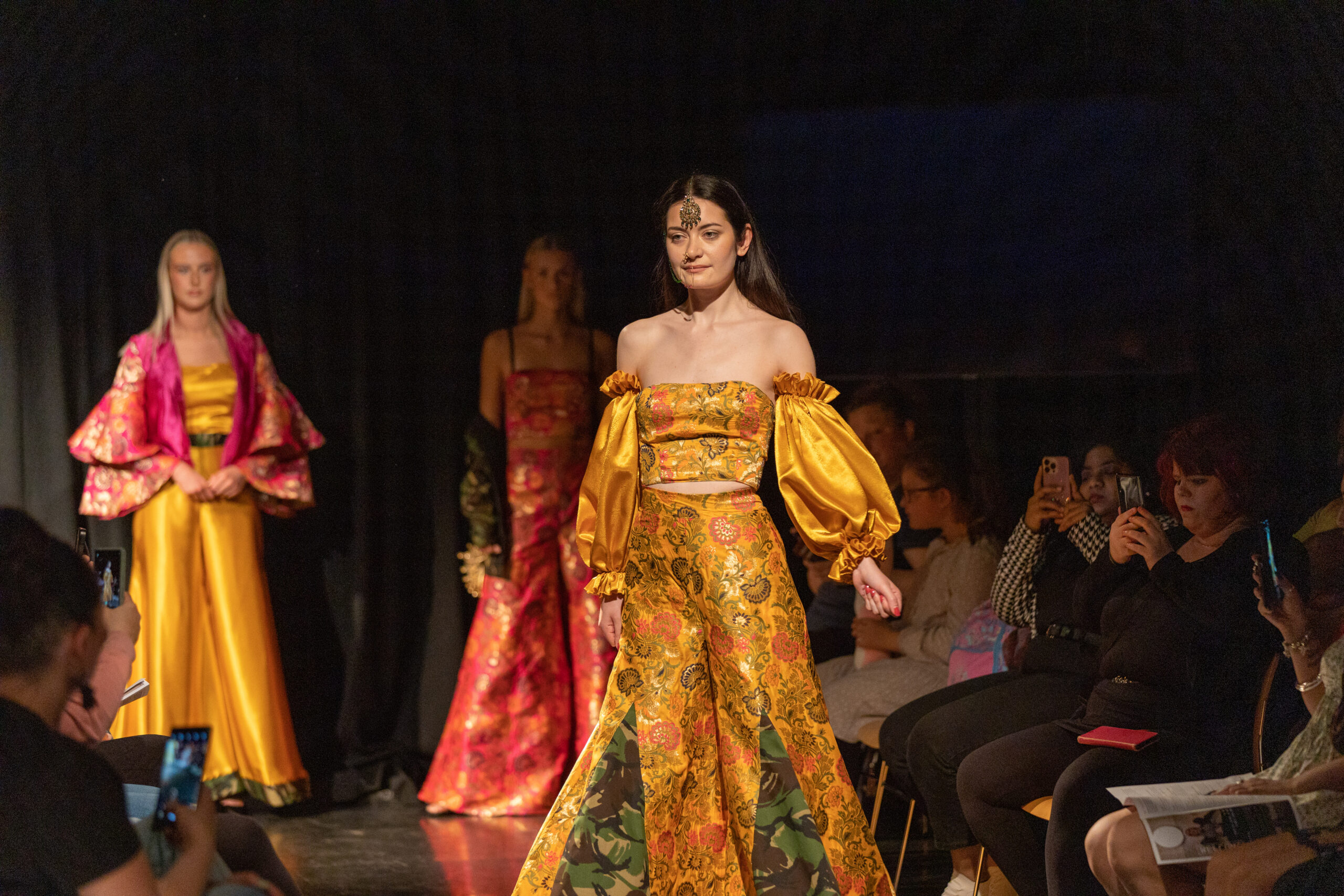 a model walks down the catwalk wearing a yellow satin top and bottoms with traditional south asian jewellery